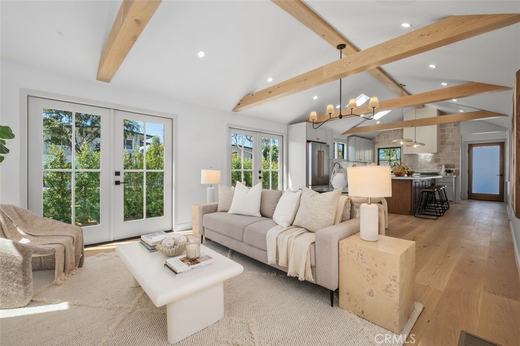 Open-plan living room with French doors, exposed timber ceiling beams, and a kitchen beyond.
