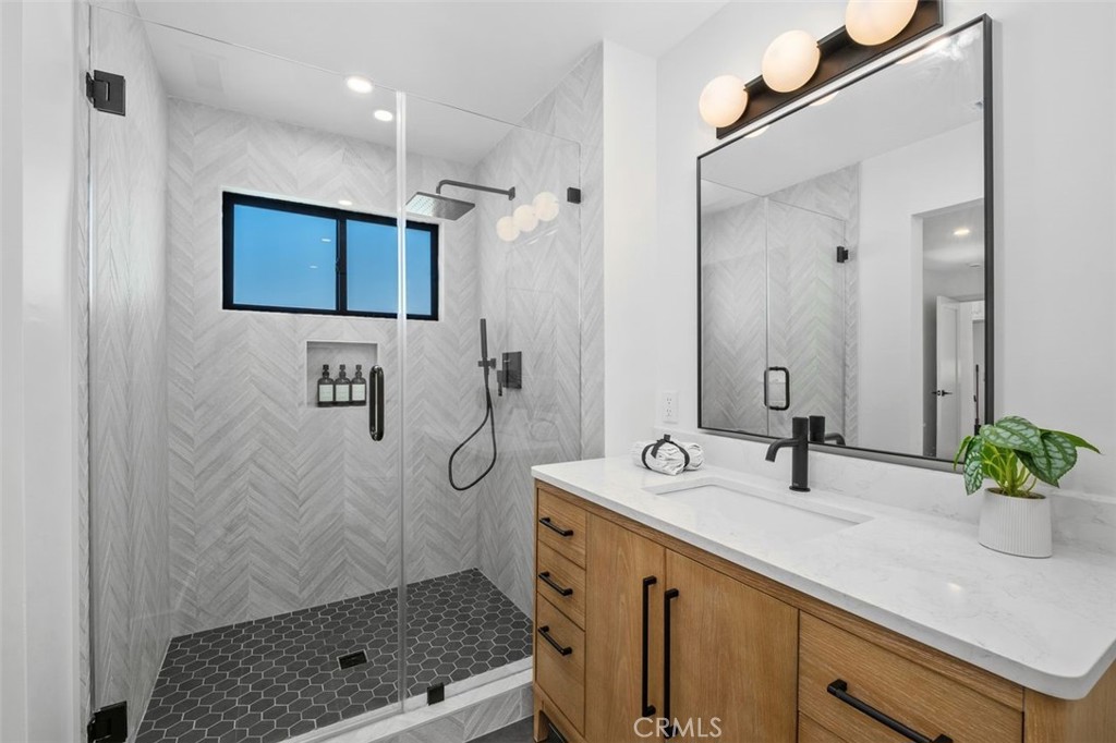 Modern bathroom with a glass walk-in shower, herringbone tile, and wood vanity.