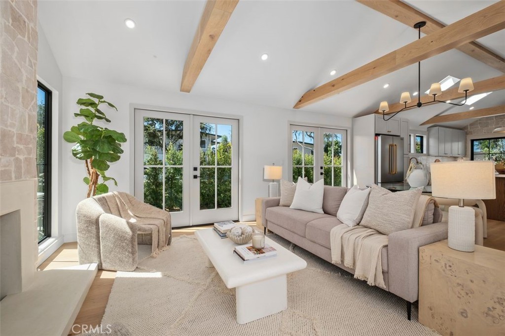 Staged living room with exposed wood beams, a stone fireplace, and glass doors opening to greenery.