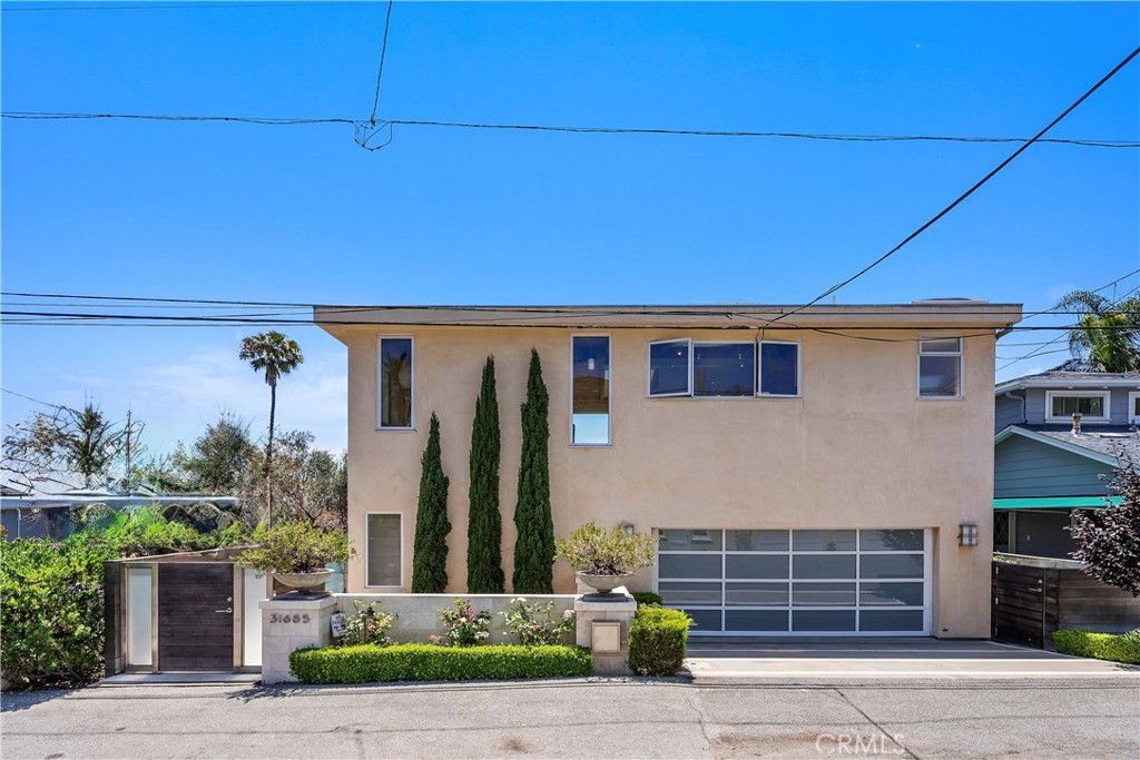 Two-story stucco home with a wide garage, gated entry, and cypress trees at the front.