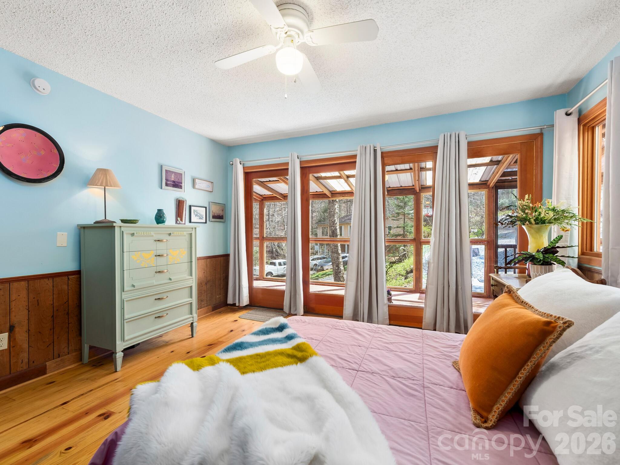 Bedroom with wood-framed windows, white curtains, blue walls and hardwood floors.