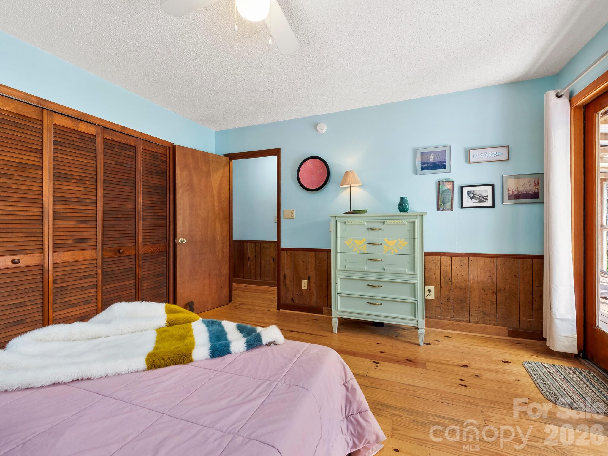 Bedroom with a pink bedspread, colorful throw, louvered closets, and pale green dresser.