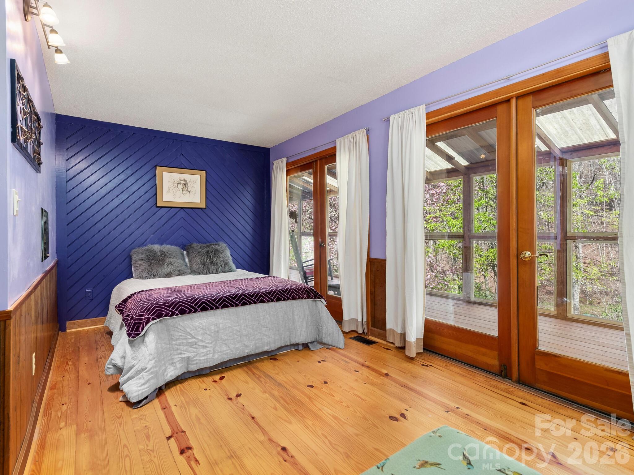 Bedroom with a blue paneled accent wall, pine floors, and glass doors opening to a covered deck.