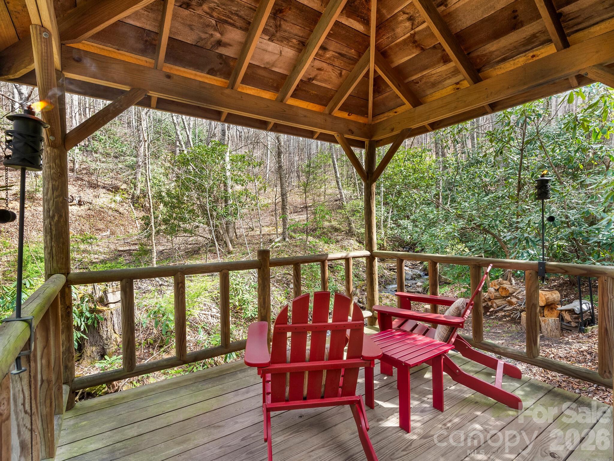 Covered timber deck with red Adirondack chairs overlooking a wooded hillside and stream.