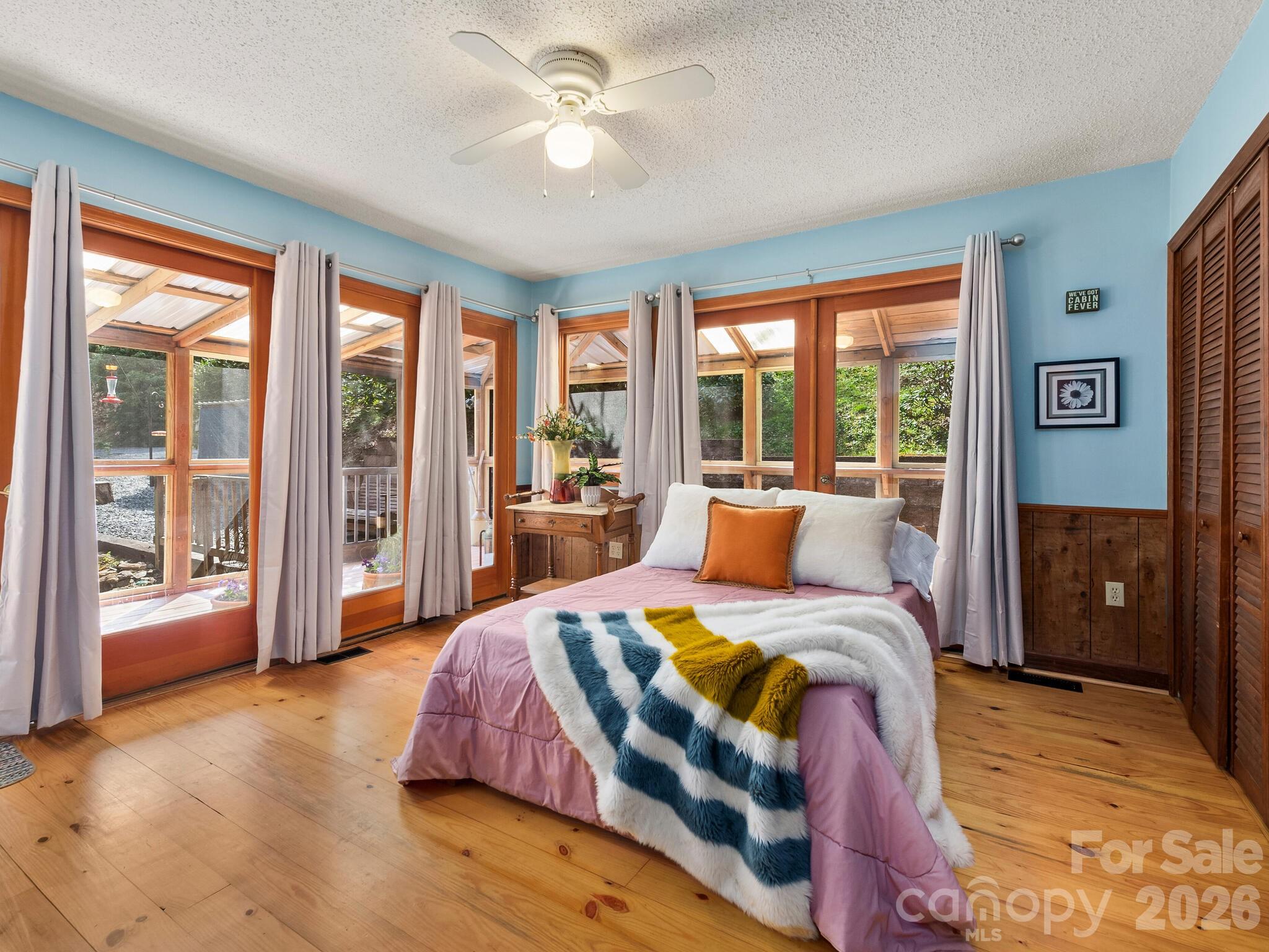 Bedroom with pink bedding, a colorful throw, and broad windows opening onto a covered porch.