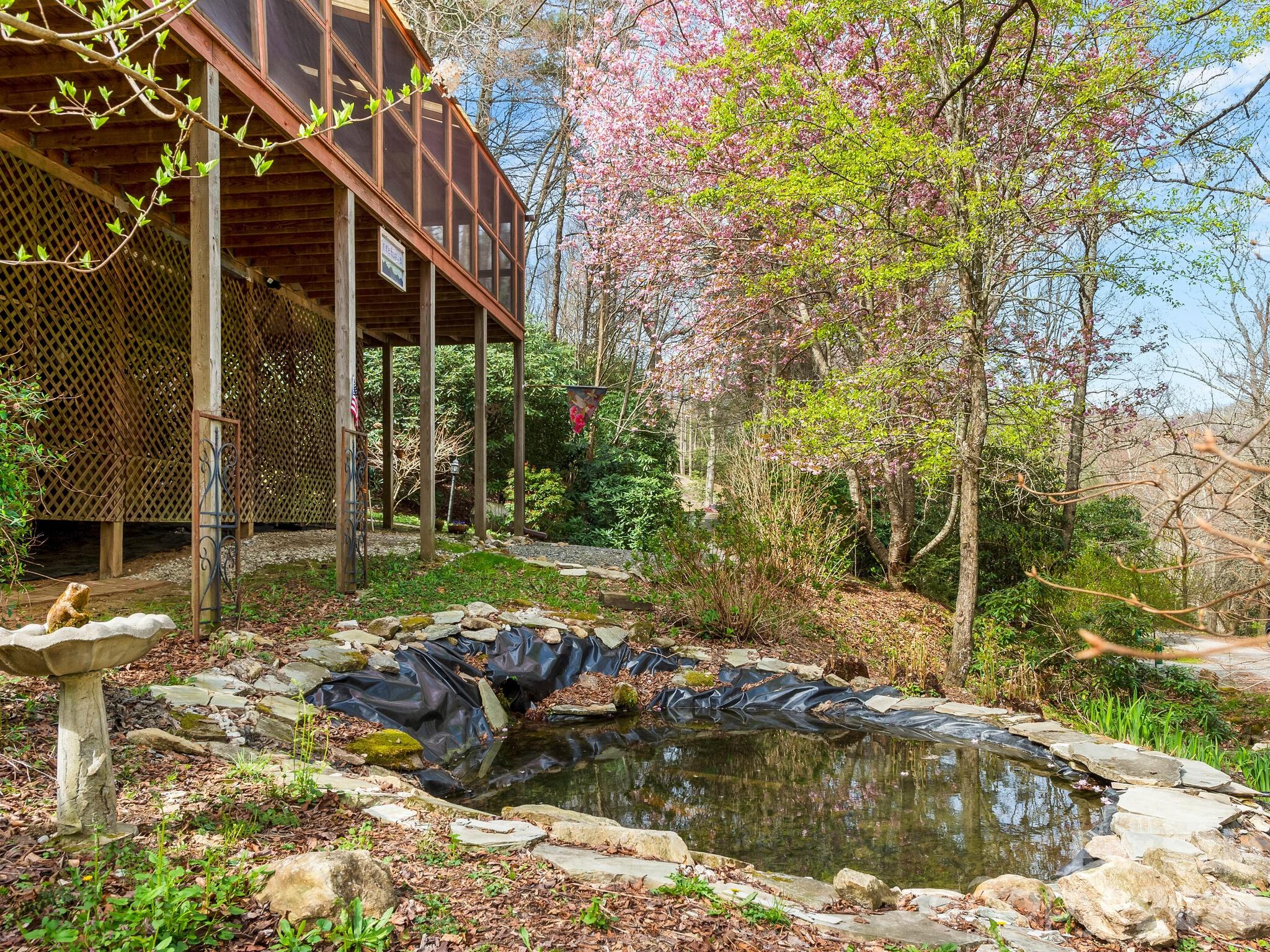 Raised wood home and screened porch beside a stone-edged garden pond and flowering trees.