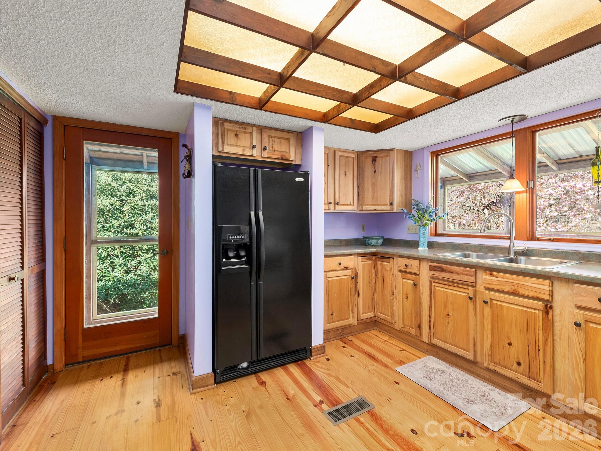 Kitchen with pine cabinets and flooring, a black refrigerator, and a wood-beamed ceiling.