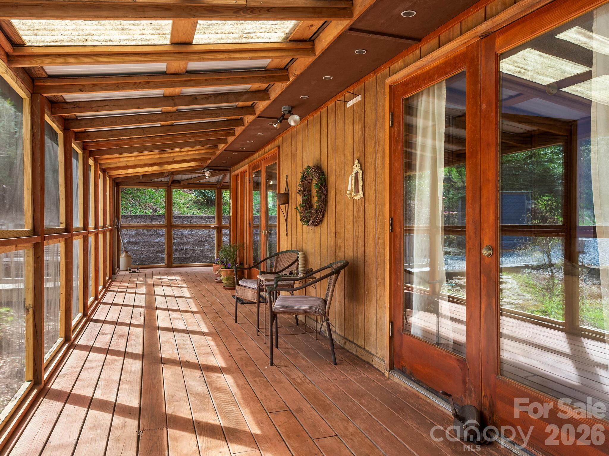 Enclosed wooden porch with exposed beams, screened windows, and two chairs beside glass doors.