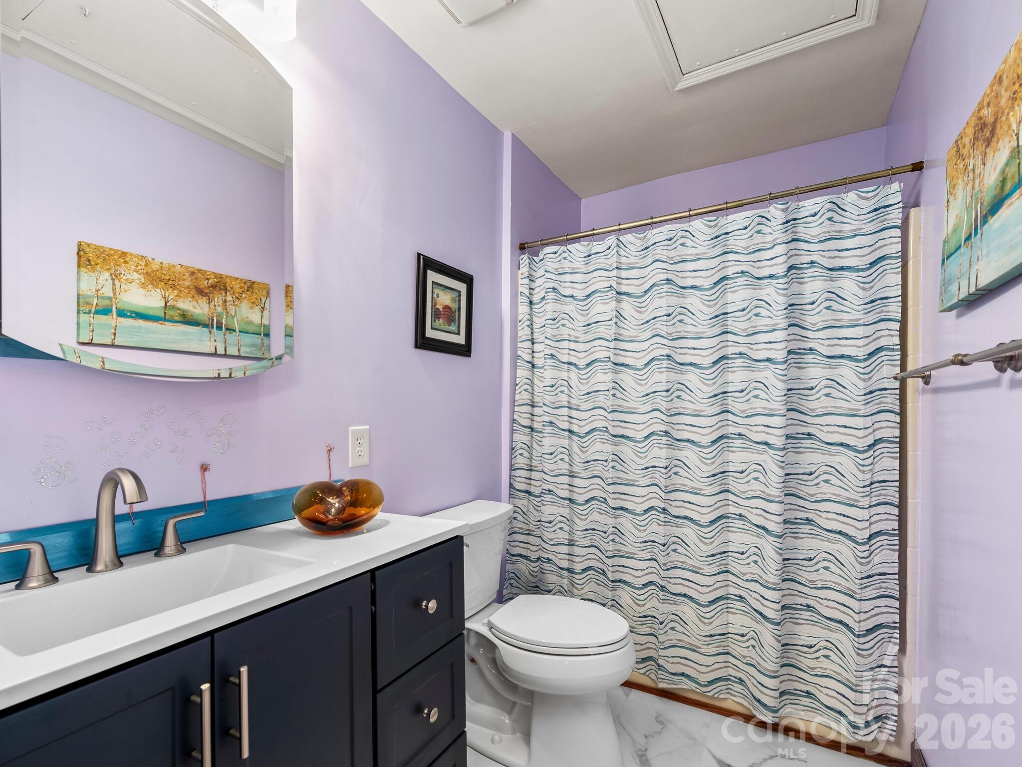 Bathroom with lavender walls, navy vanity, amber vessel sink, and blue-and-white wavy shower curtain.
