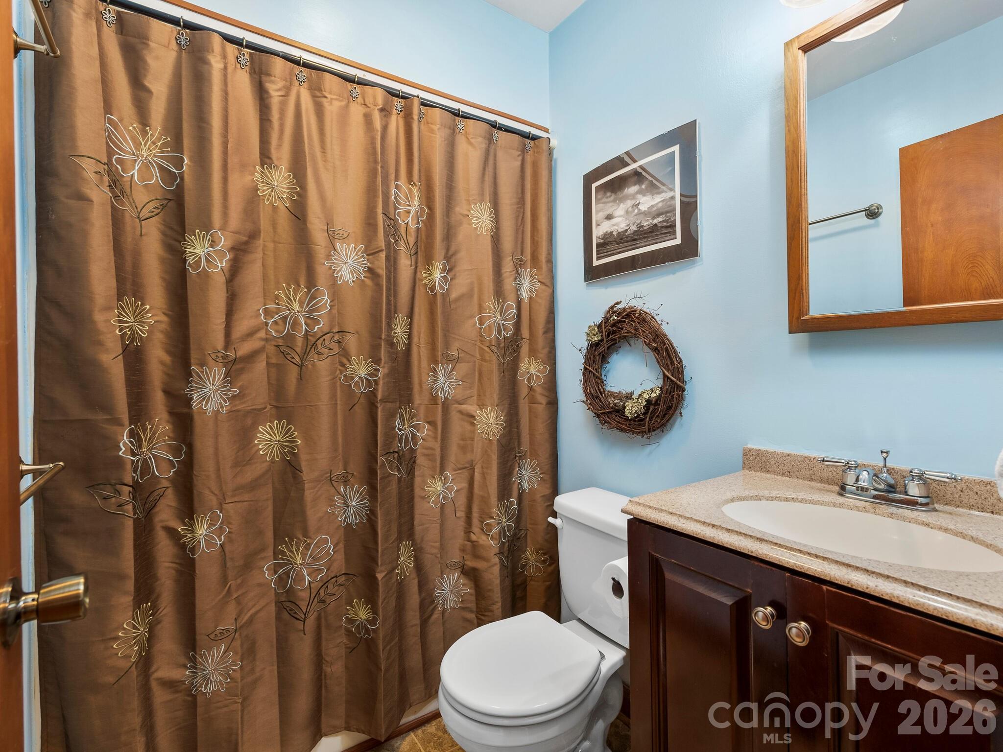Bathroom with a brown floral shower curtain, white toilet, and dark wood vanity with a stone countertop.