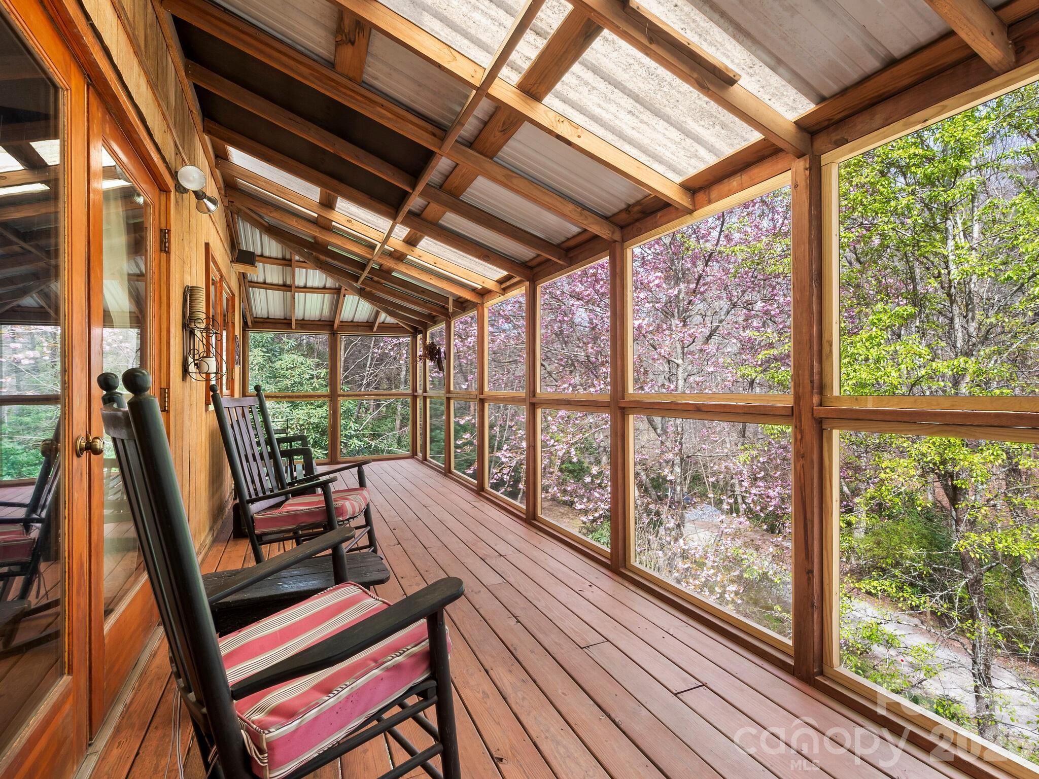 Screened wooden porch with cushioned rocking chairs and views of flowering trees.