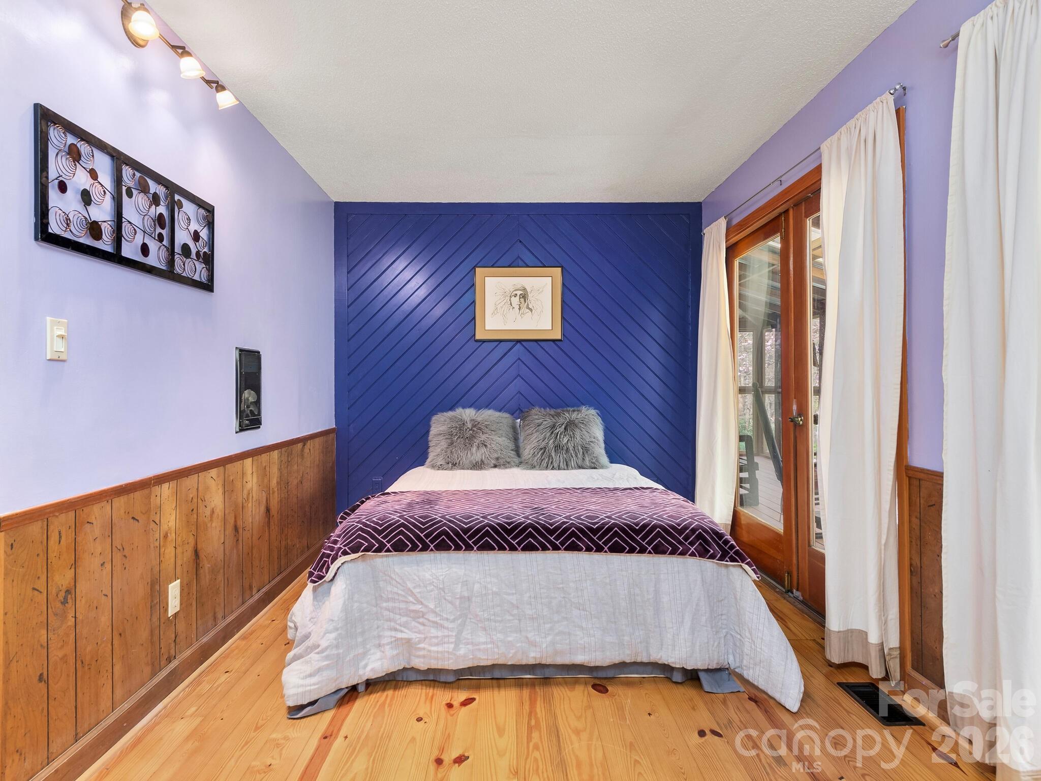 Bedroom with a blue chevron accent wall, wood floors, and glass doors with white curtains.