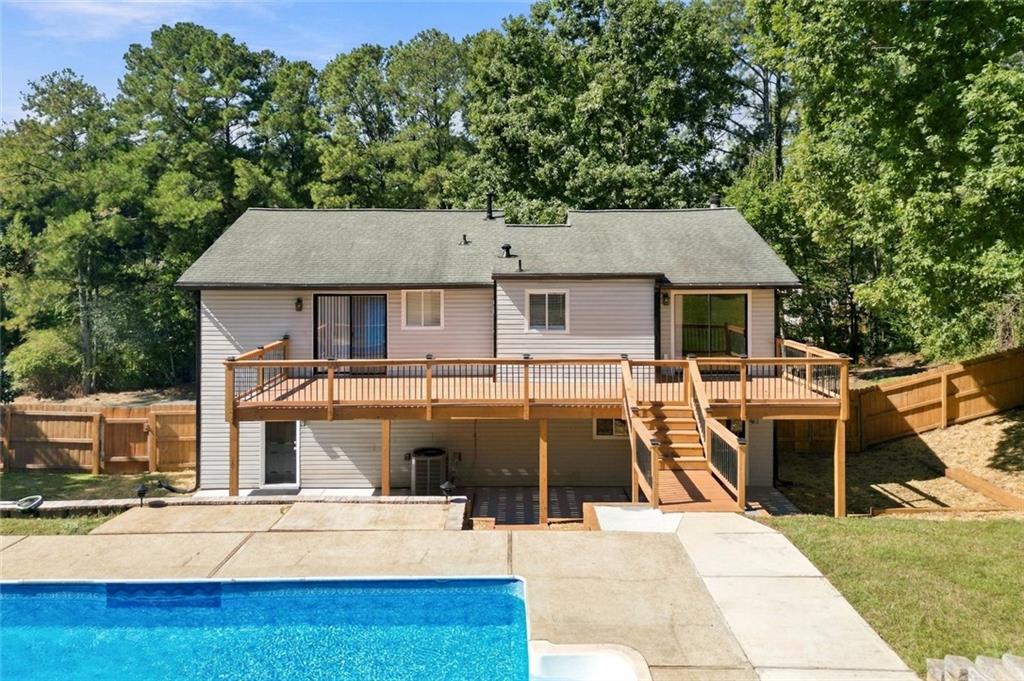 House rear with raised wooden deck, fenced yard, and swimming pool.