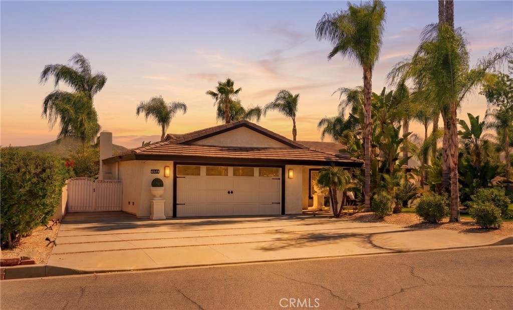 Single-story home with a tiled roof, double garage, and palm trees at sunset.