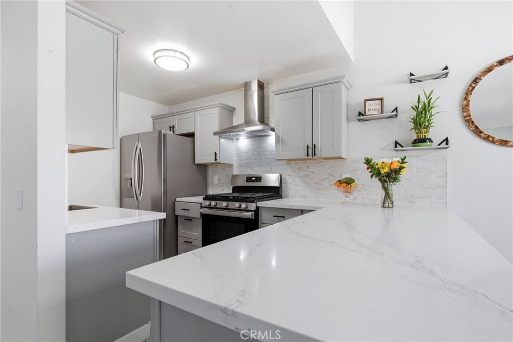 Kitchen with gray cabinets, stainless steel appliances, and a large white marble-look peninsula.