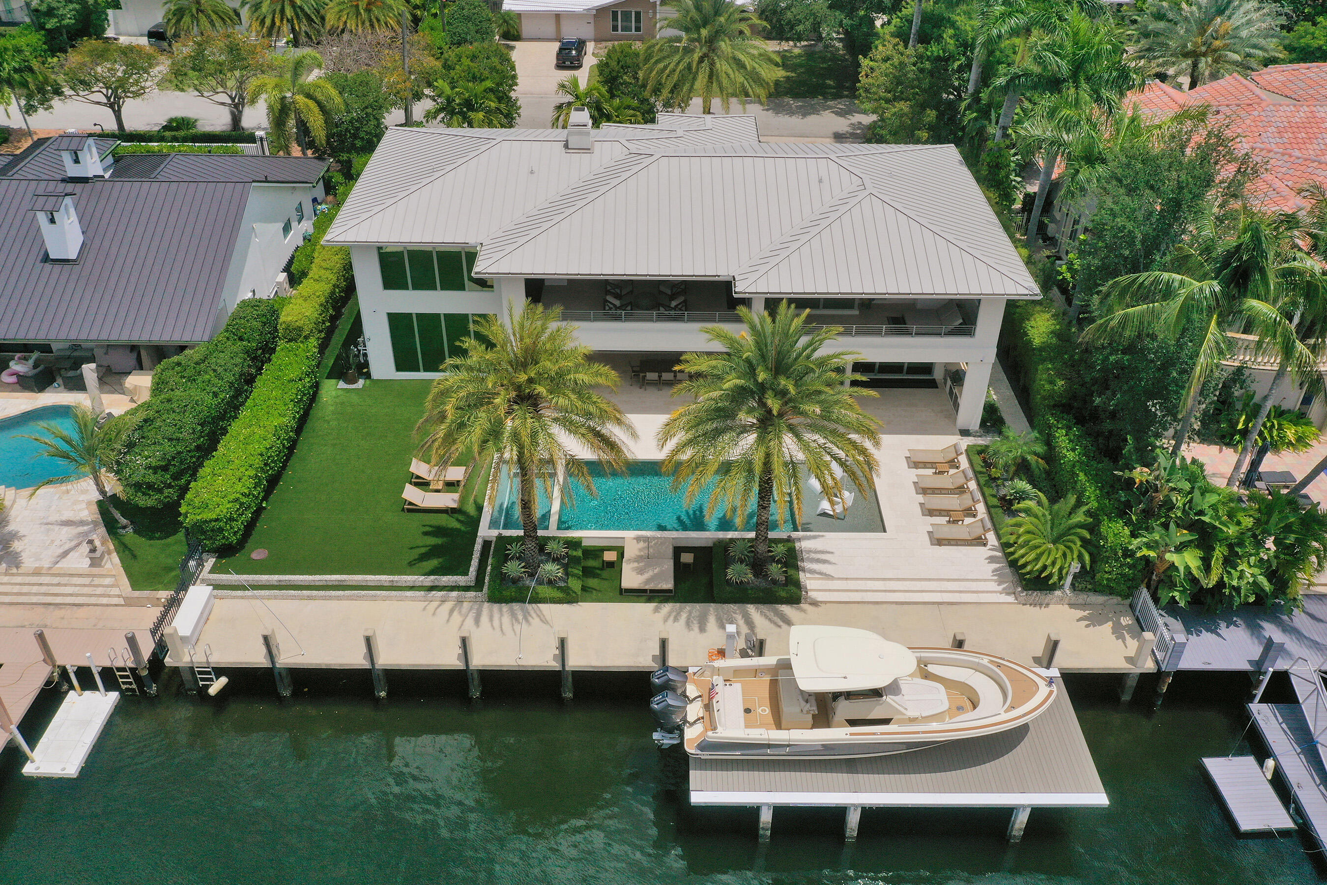 Aerial view of a modern waterfront home with a pool and boat at its dock.