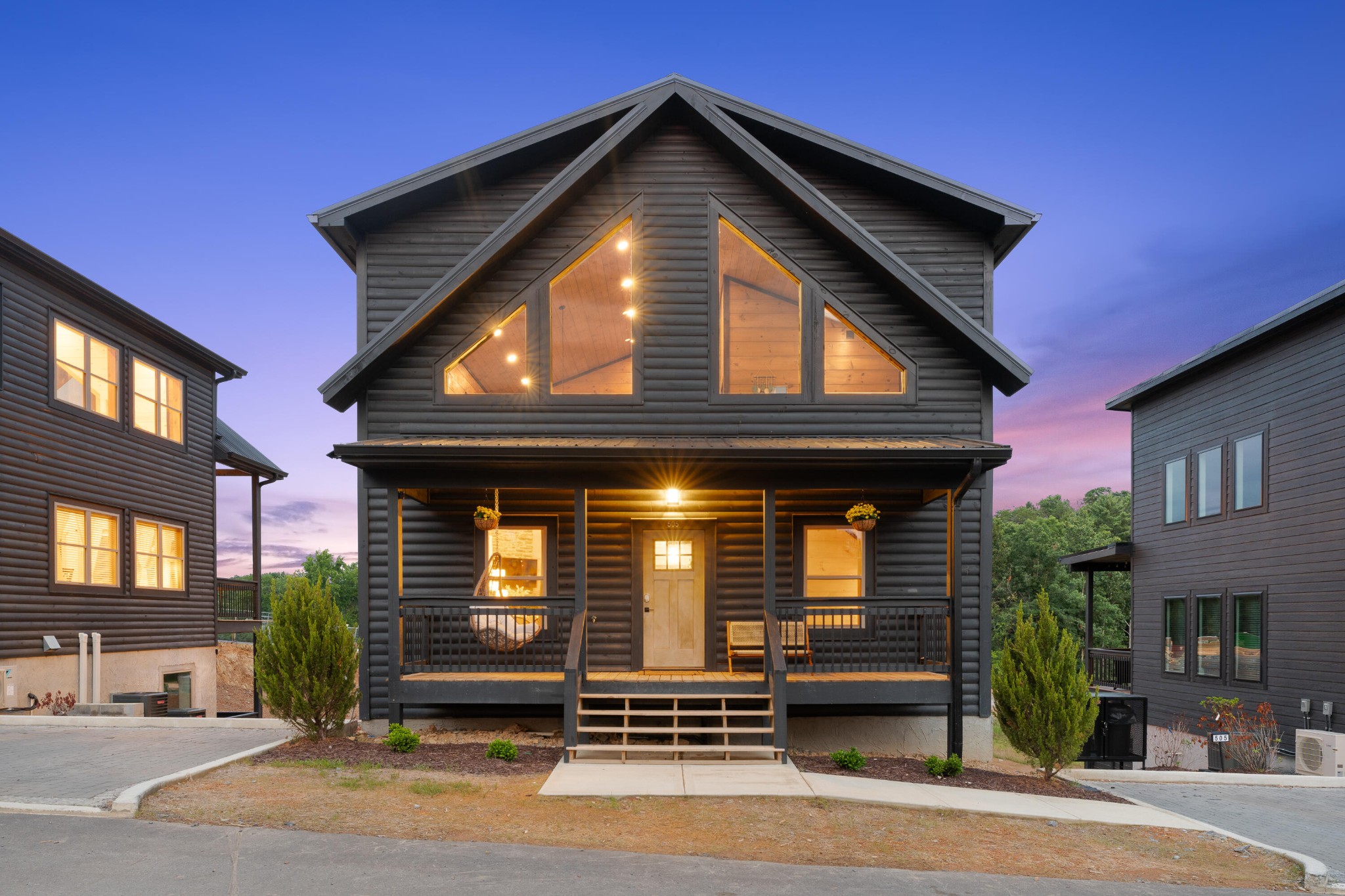 Two-story log-style house at dusk with a steep roof, glowing windows, and a covered front porch.