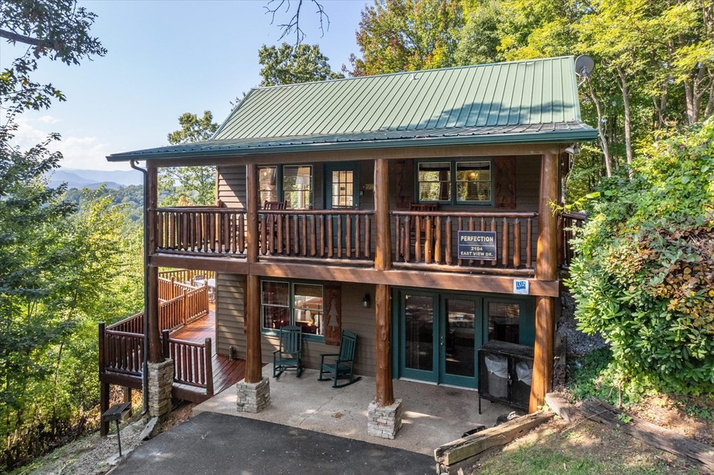 Wood-sided mountain home with a green metal roof, covered porch, and wooded mountain view.