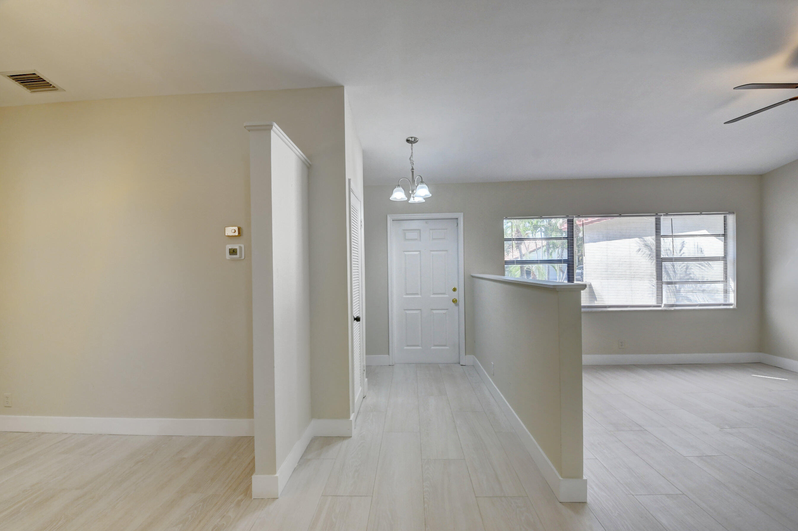 Empty entry foyer opening into a living area with light tile floors and wide windows.