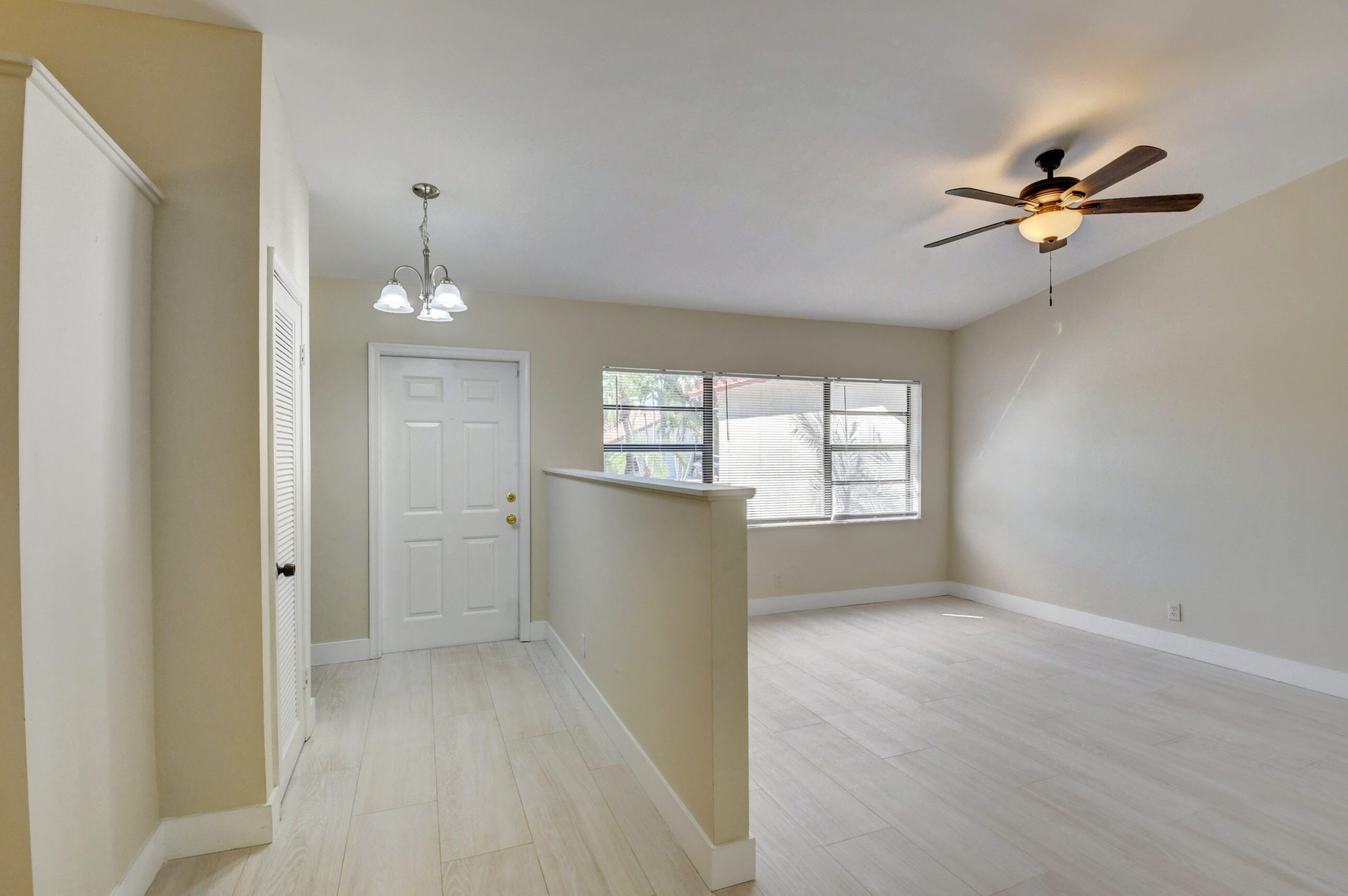 Vacant living area with pale tile floors, a ceiling fan, and a window with blinds.