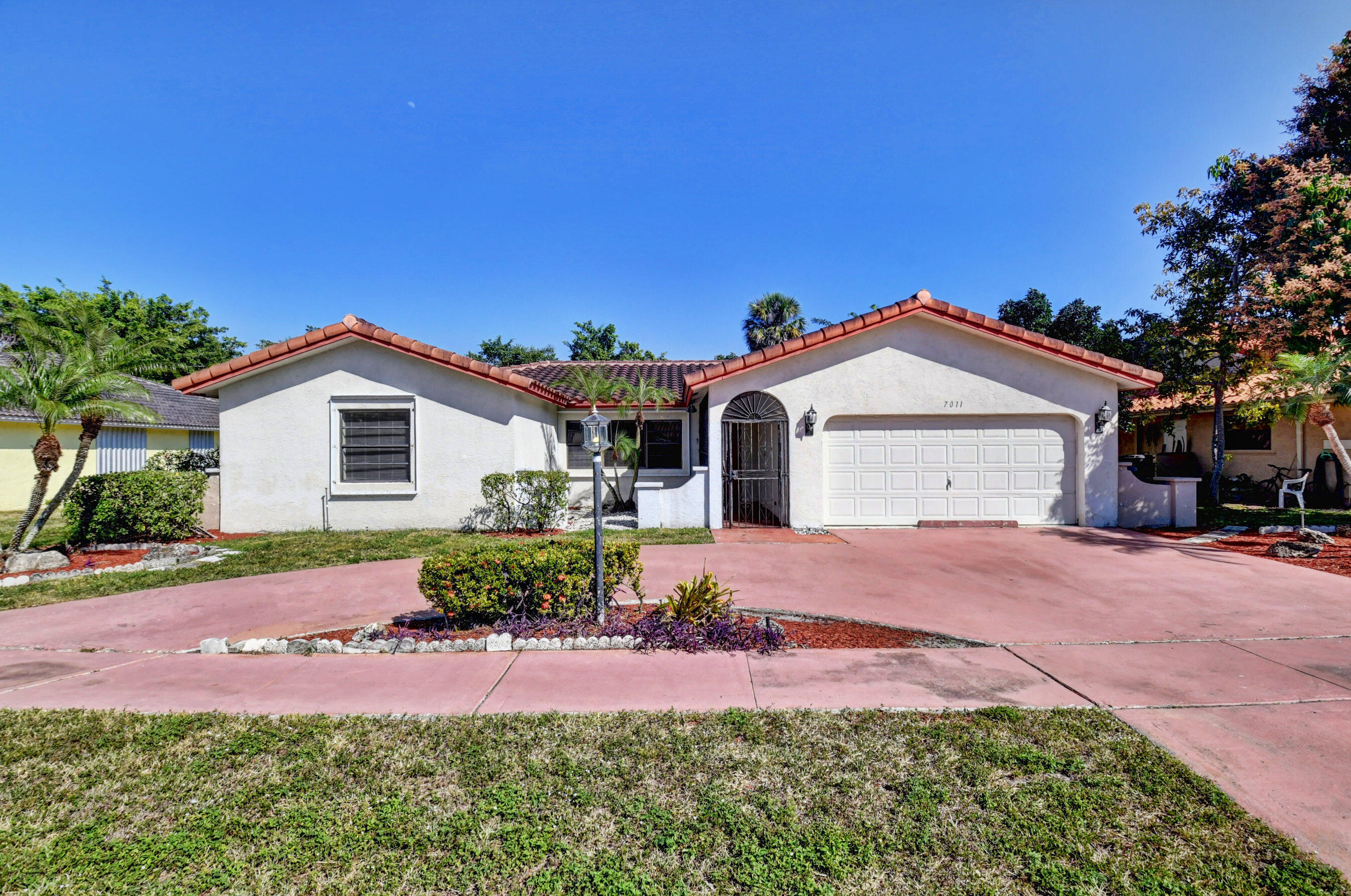 Single-story white stucco home with red tile roof, arched entry, and wide pink driveway.