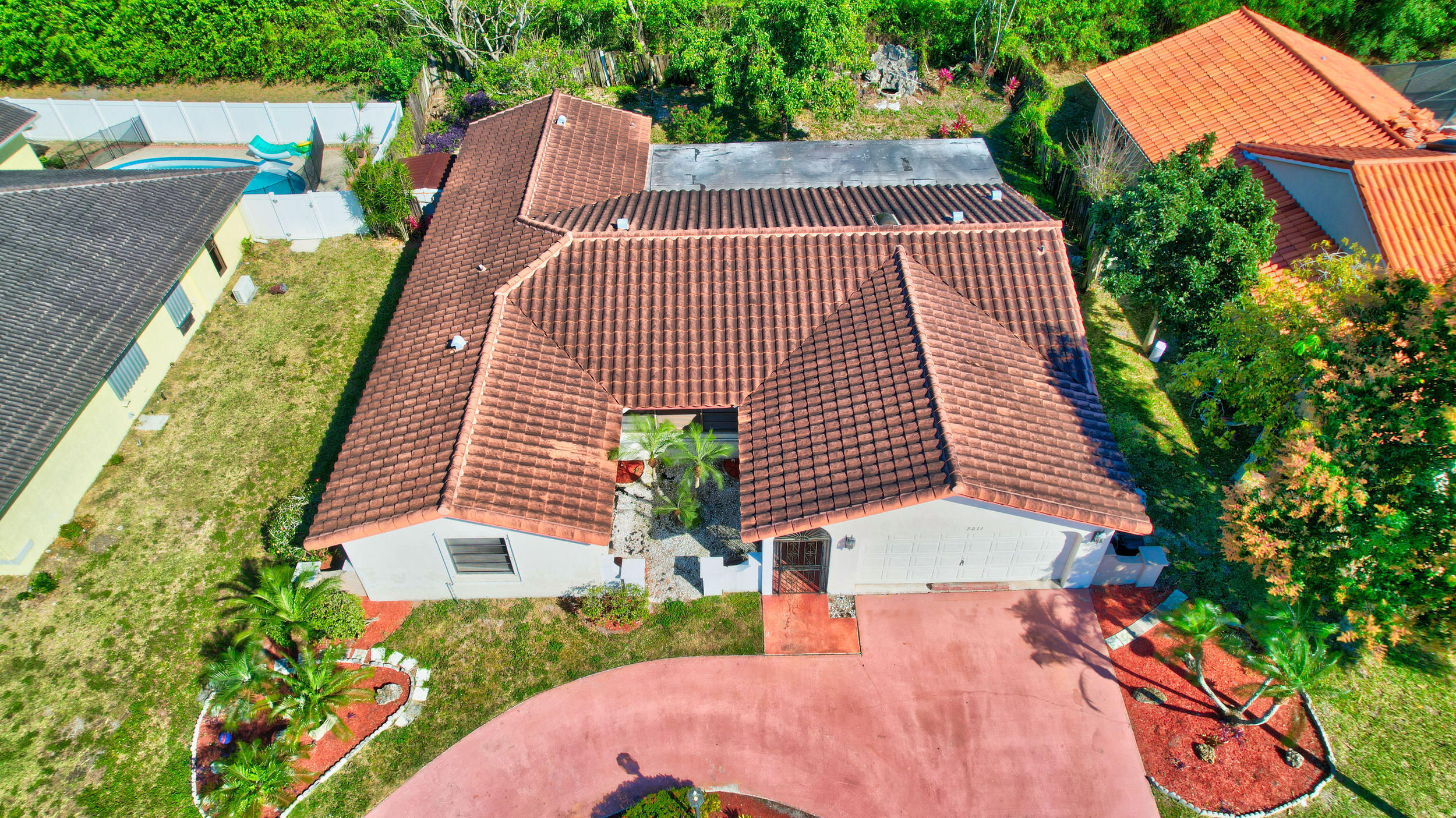 Aerial view of a red tile-roofed home with a curved driveway and landscaped front yard.