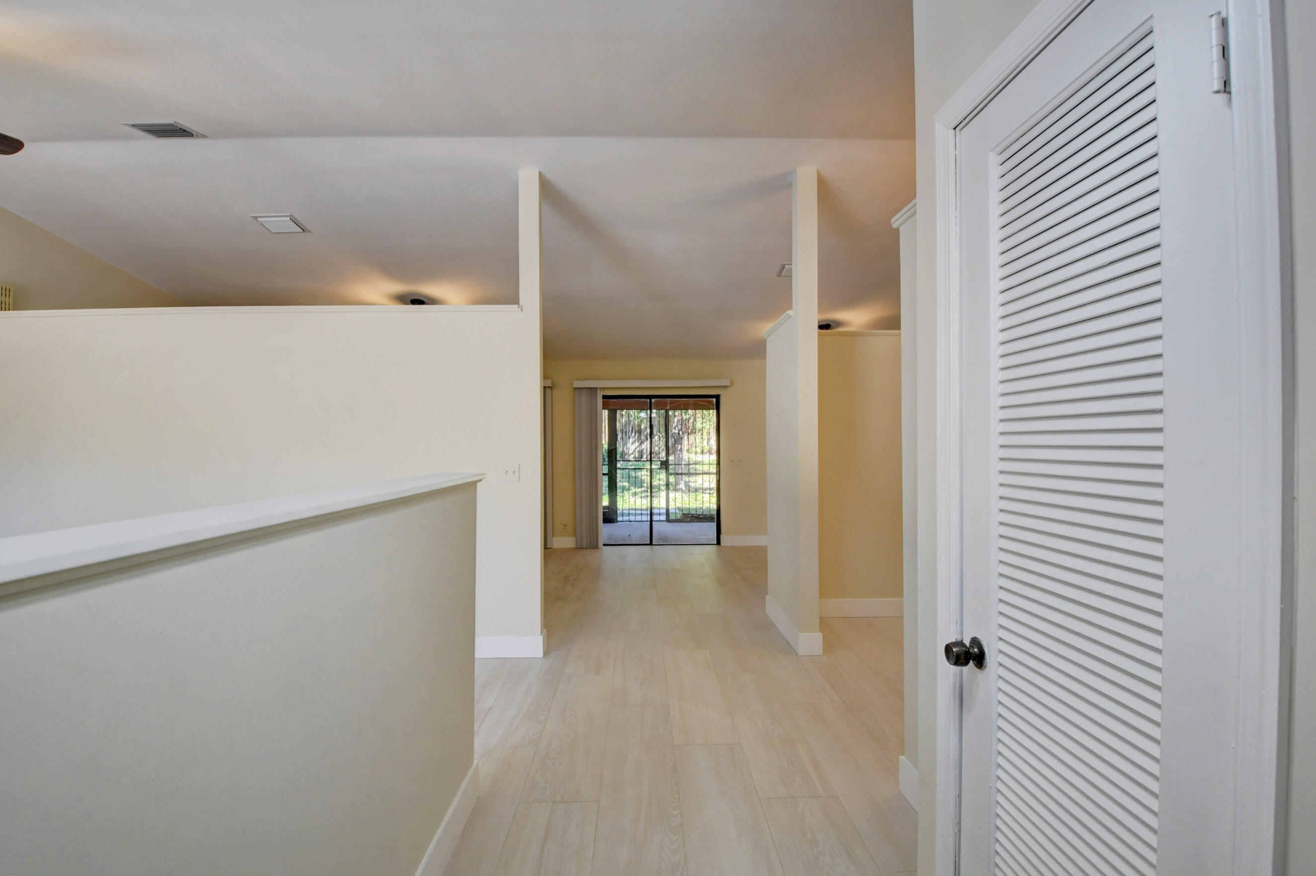 Open hallway with light tile flooring leading to sliding glass doors; white louvered door at right.
