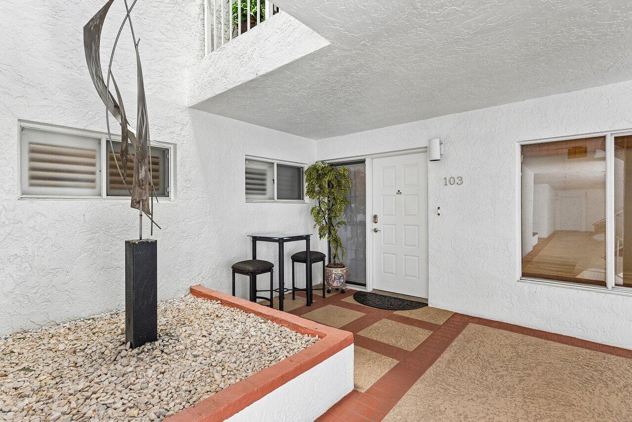 Condo entrance with a tiled walkway, gravel courtyard, and metal sculpture beside unit 103.