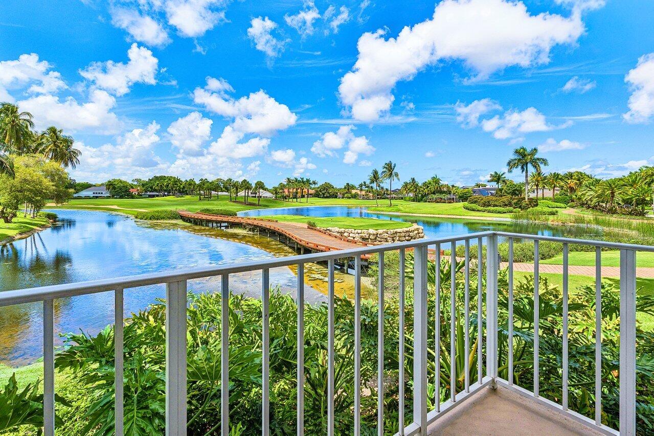 Balcony overlooking a lake and golf course, with a wooden footbridge and palm trees.