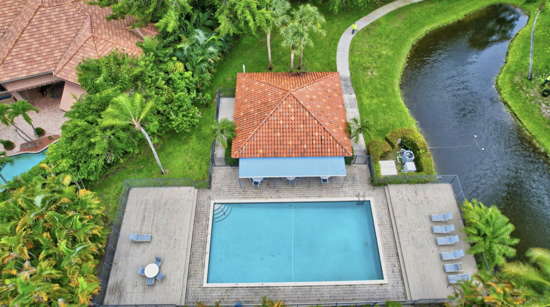Aerial view of a swimming pool and deck beside a tiled-roof pavilion and canal.