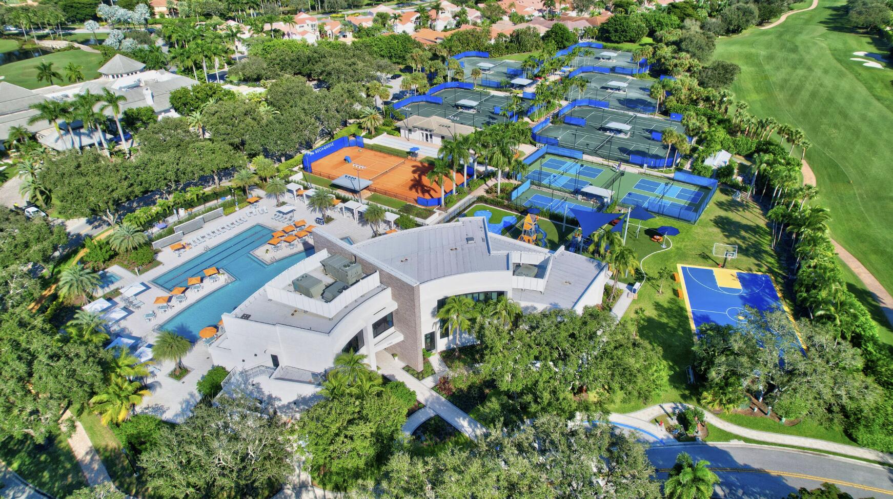 Aerial view of a community clubhouse, pool, tennis courts, basketball court, and adjacent golf course.