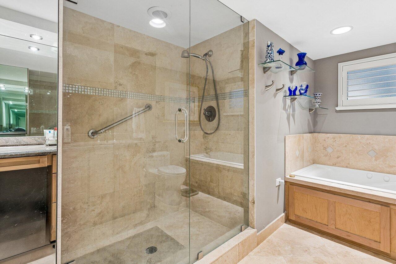 Bathroom with a glass-enclosed stone-tile shower, built-in jetted tub, and blue glass decor.