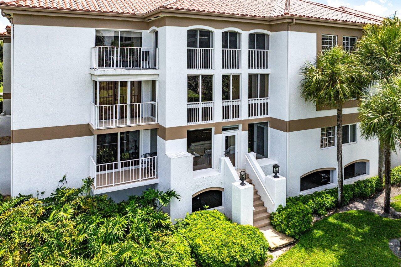 White condominium building with multiple balconies, a tiled roof, and a central entrance staircase.