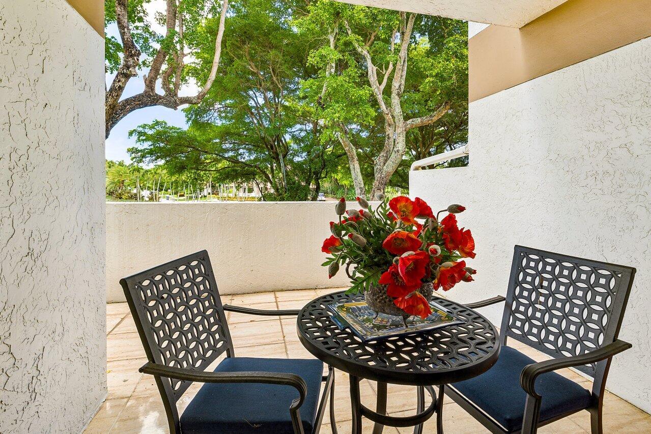 Covered patio with black metal seating, red flowers, and leafy trees beyond the wall.