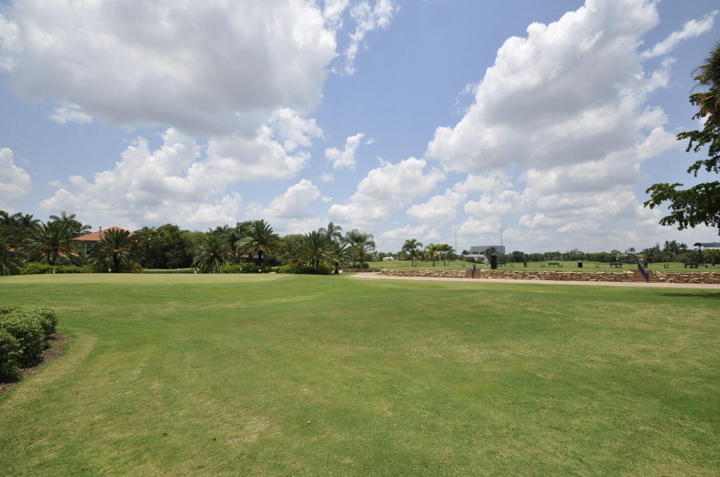 Broad green lawn with palm trees and a low stone wall beneath a cloud-filled sky.