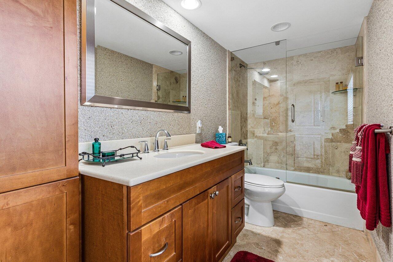 Bathroom with a wood vanity, large mirror, and glass-enclosed tub and shower.