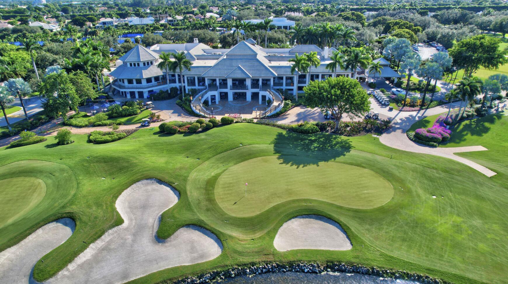 Aerial view of a clubhouse beside putting greens, bunkers, and landscaped grounds.