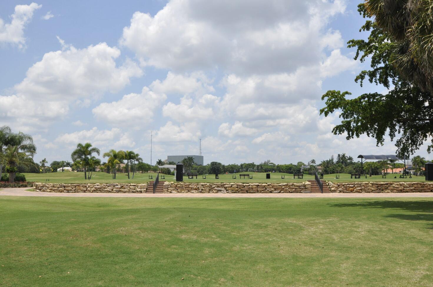 Community recreation lawn with benches, palm trees, and a low stone retaining wall.