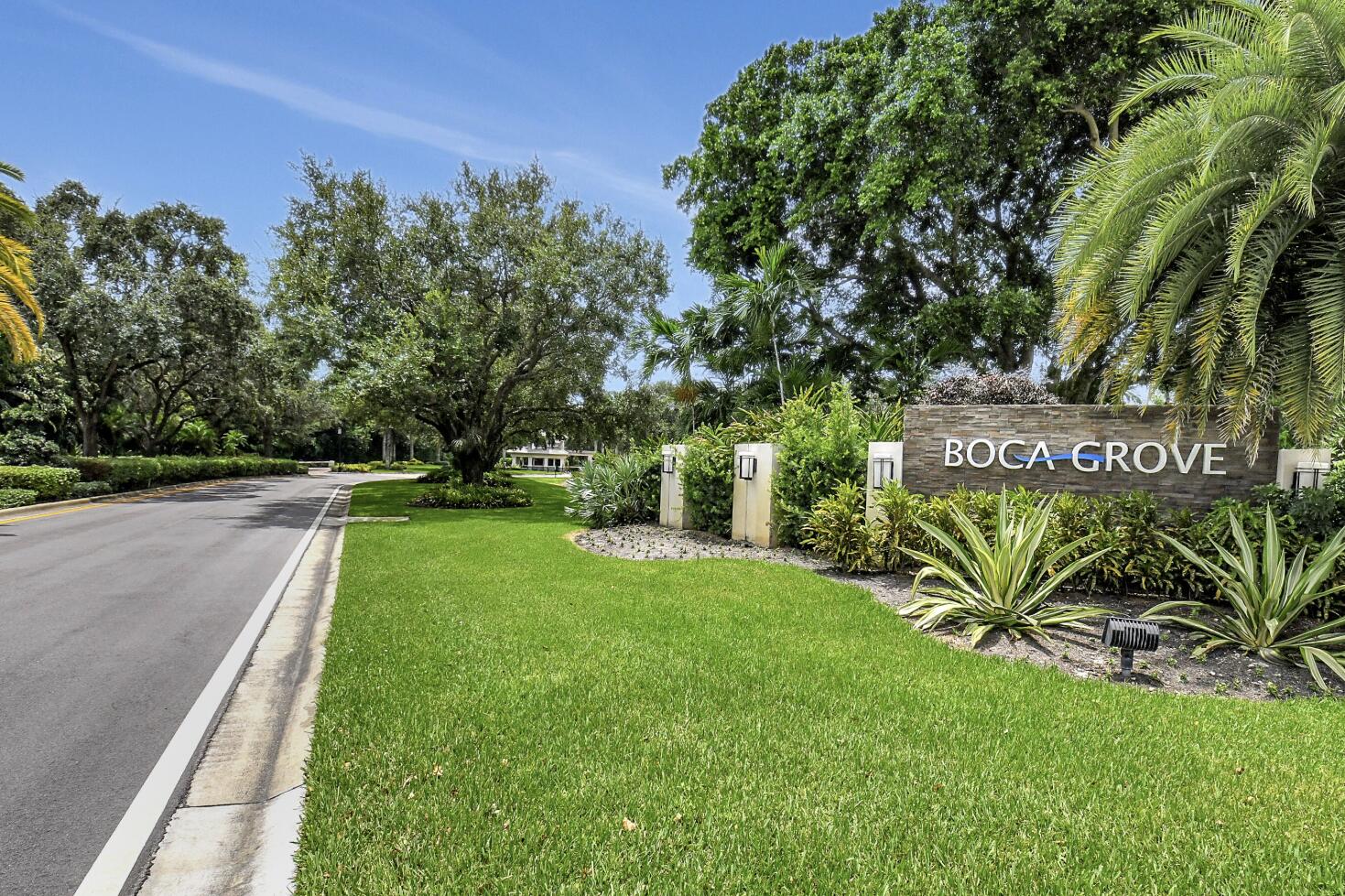 Boca Grove community entrance with stone monument sign, landscaped lawn, and tree-lined roadway.