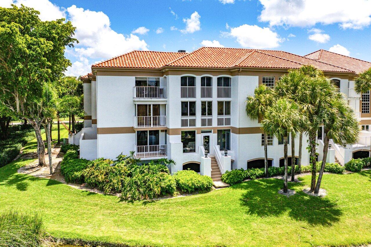 Condominium building with a terracotta tile roof, stacked balconies, and palm trees in the landscaped grounds.