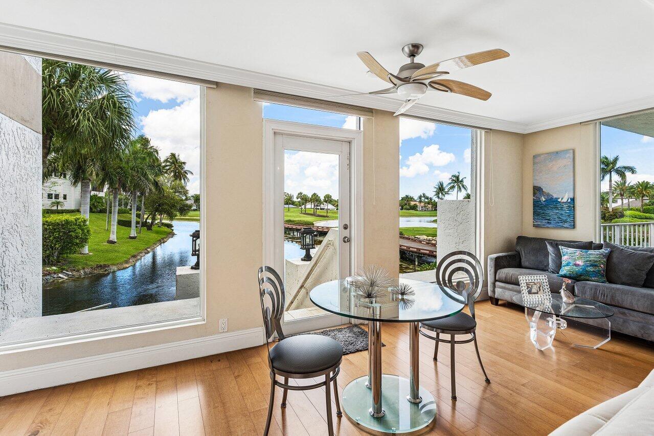 Living and dining area with a glass table and large windows overlooking a palm-lined canal.
