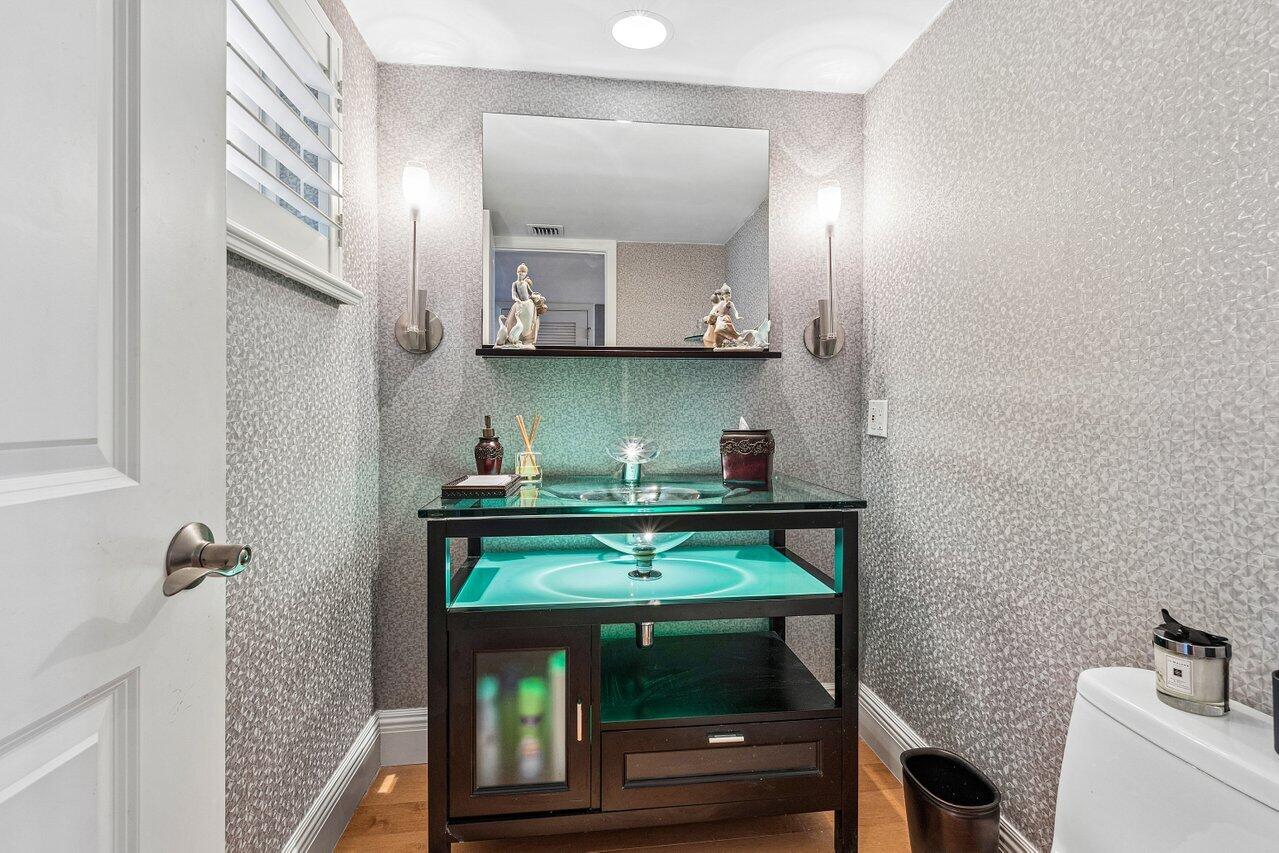 Powder room with textured gray wallpaper and a turquoise-lit glass vessel sink vanity.