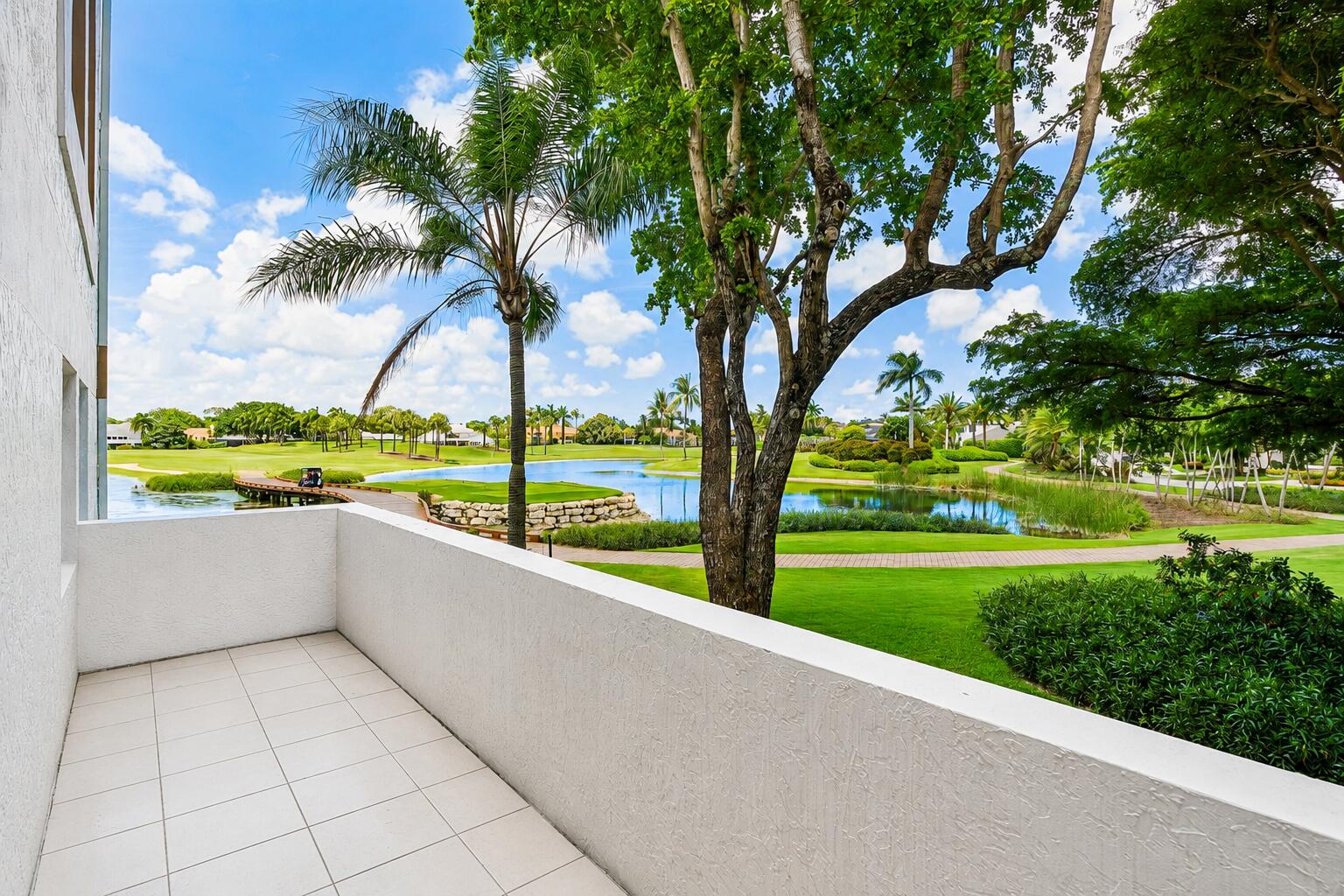Balcony overlooking a golf course and pond, framed by a palm and large shade tree.