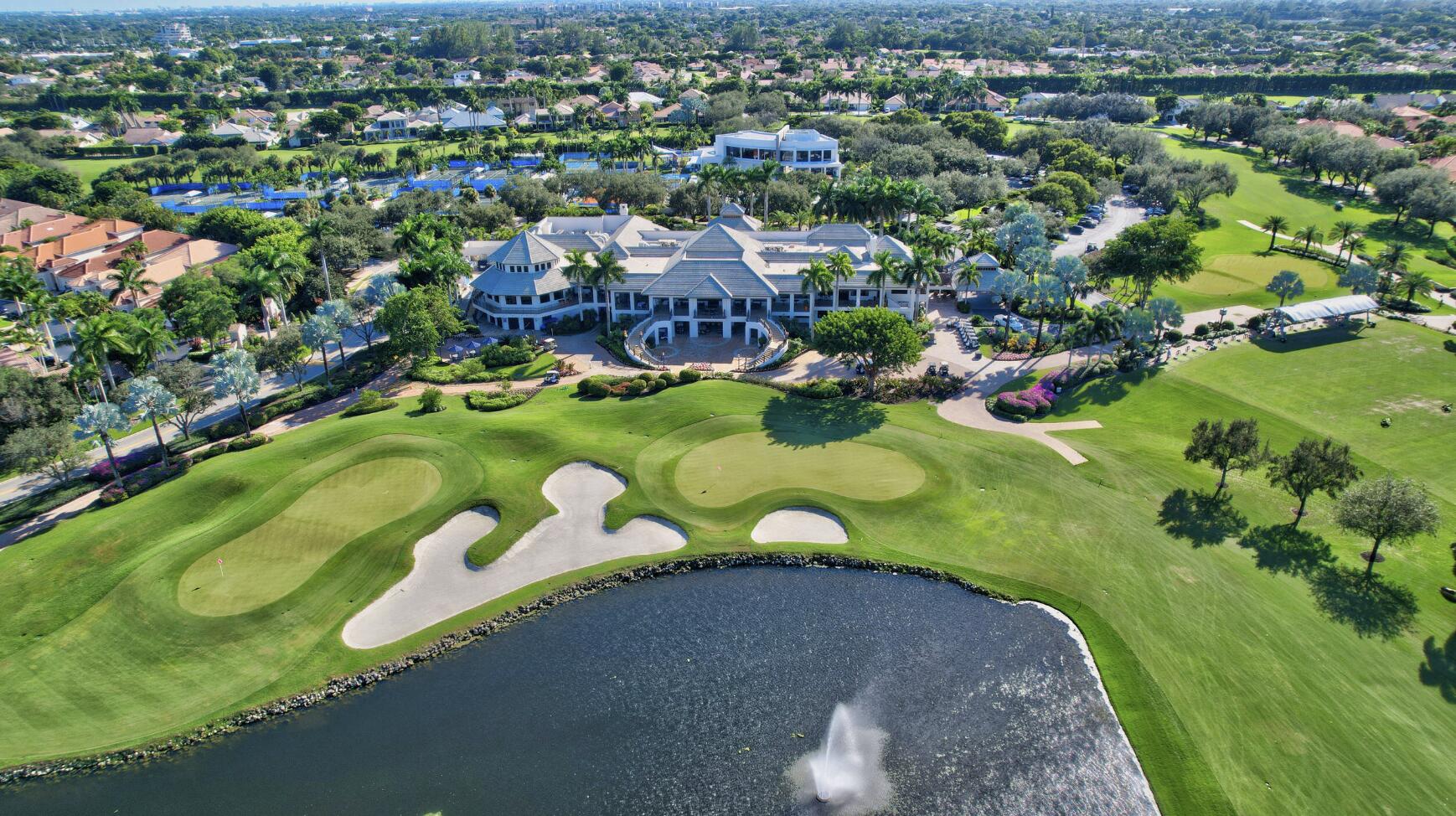 Clubhouse and golf course beside a pond with a fountain, viewed from above.