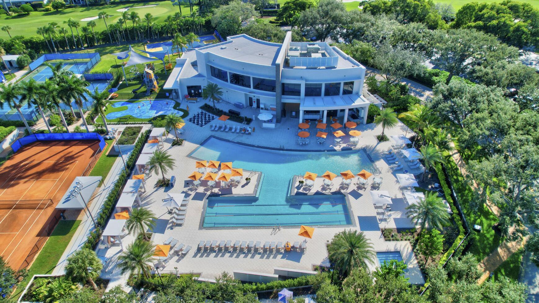 Aerial view of a condominium clubhouse, pool, tennis courts, and landscaped grounds.