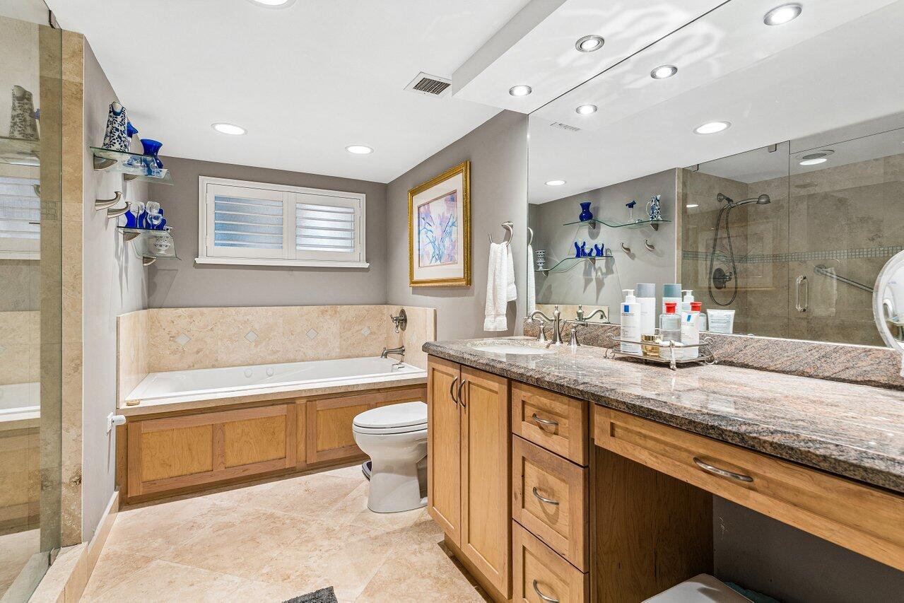 Bathroom with a soaking tub, glass shower, and long granite-topped wood vanity.