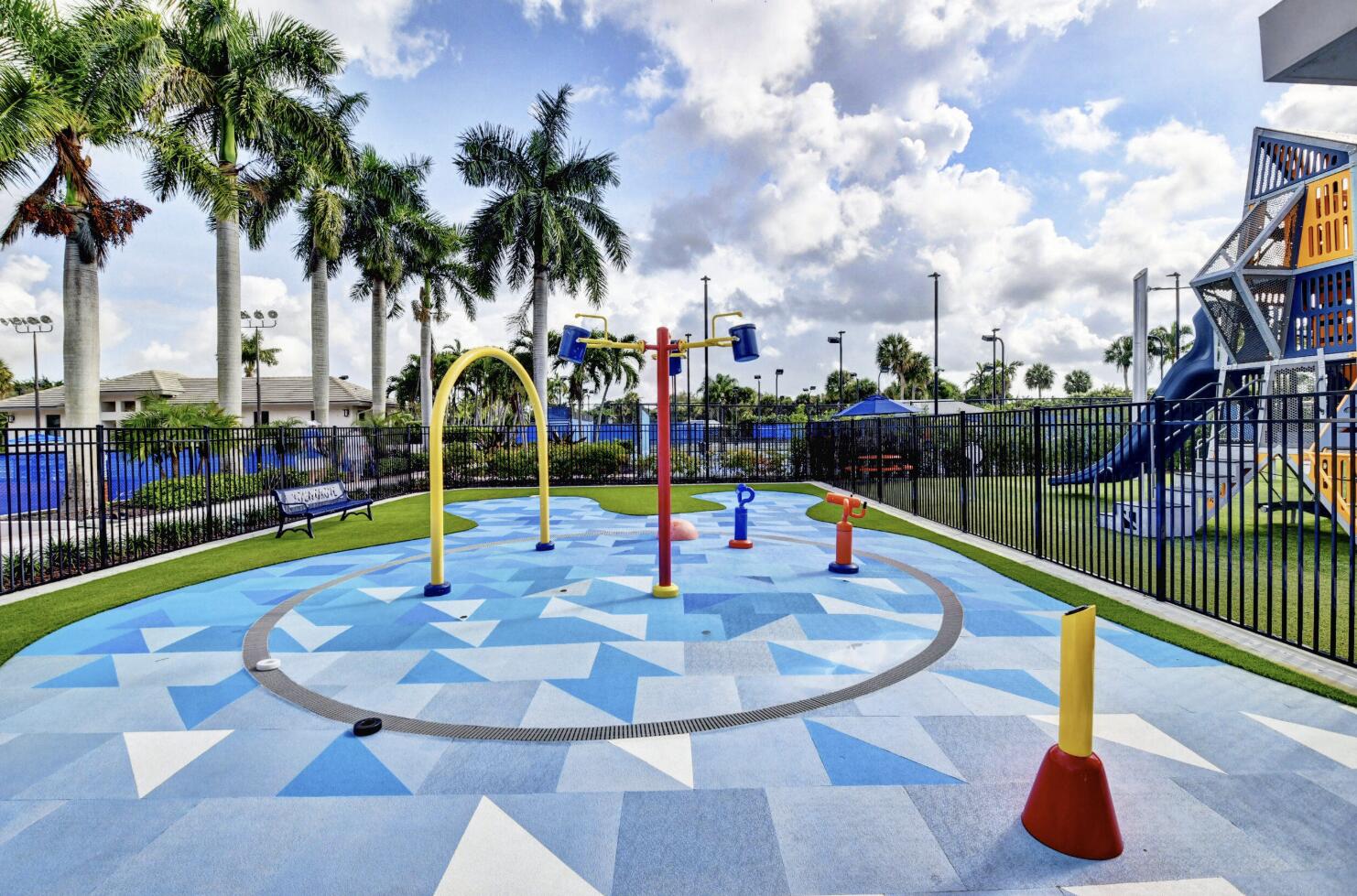 Community splash pad with colorful water-play features beside a fenced playground.