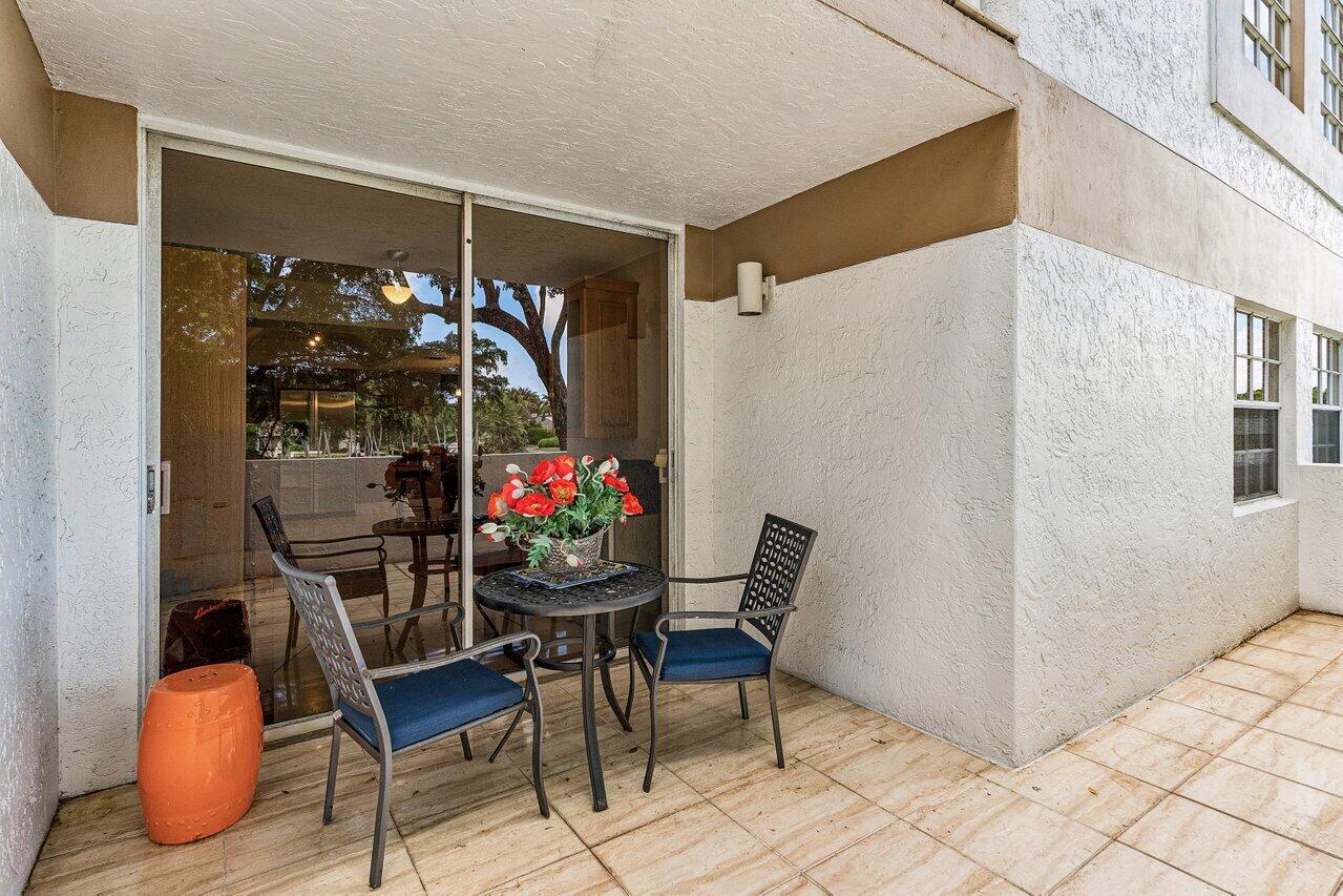 Covered condo patio with blue-cushioned chairs, a flower-topped table, and sliding glass doors.