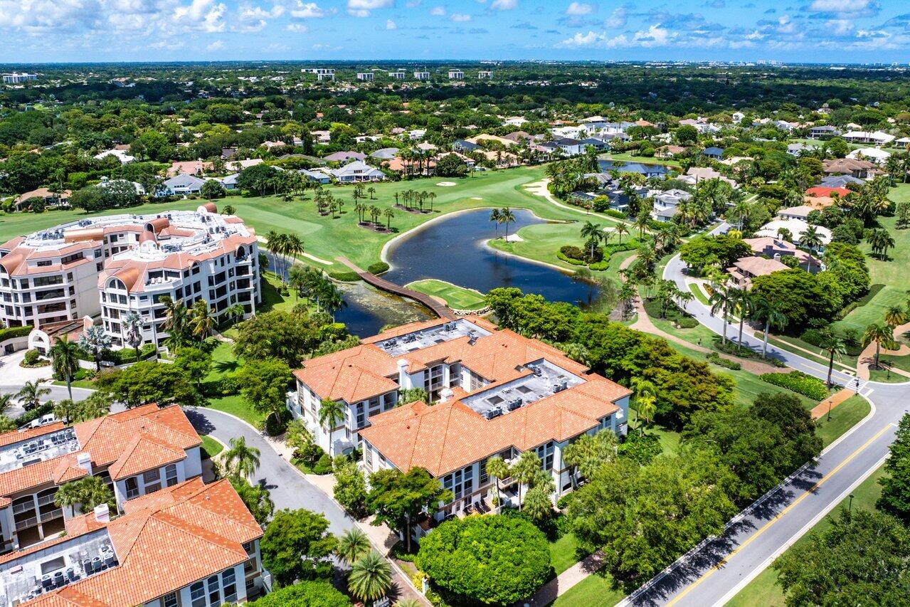 Aerial view of a condominium community beside a golf course, pond, and palm-lined fairways.