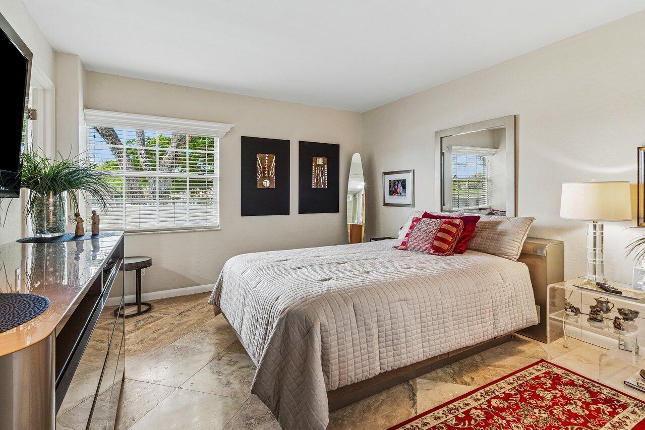 Furnished bedroom with a large light-quilted bed, red accent pillows, and a window with white blinds.